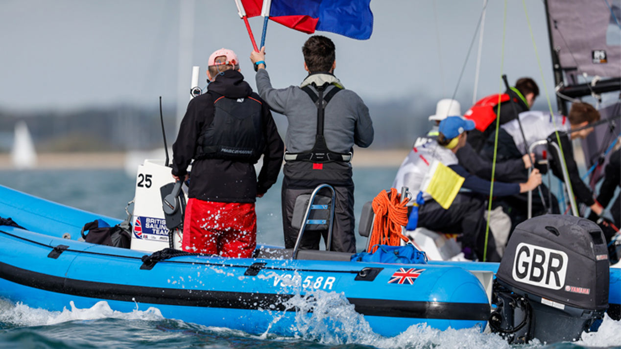 A image with two men on a boat with one being a umpire holding a red flag