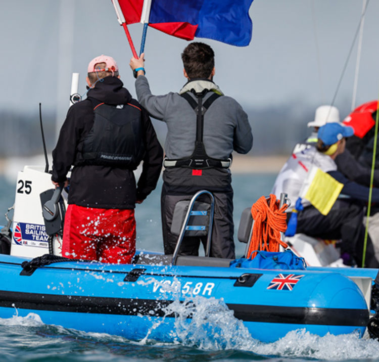 A image with two men on a boat with one being a umpire holding a red flag