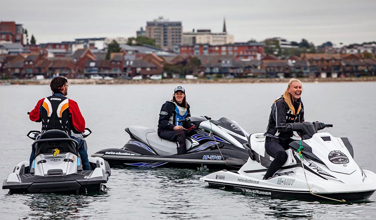 two women and one man stationary on 3 PWCs in a group on the water