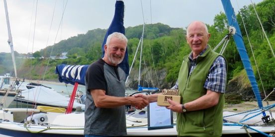 Cardigan Bay Watersports principal Crawford McLeary presents an RYA Cymru Wales Impact Award to Stephen Wood, onshore with keelboat in background.