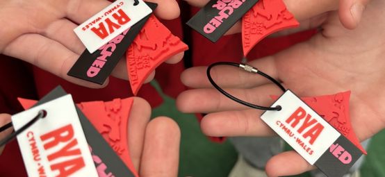 Hands of young sailors holding up the new Welsh Sail / Hwyl Cymru Awards keychain.