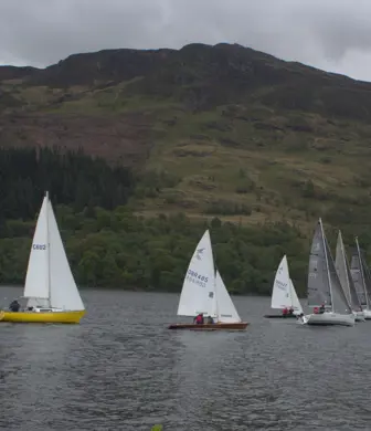A group of dinghies sailing on the water with hills in the background on a cloudy day