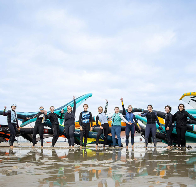 a group of wing surfing women cheering on a beach