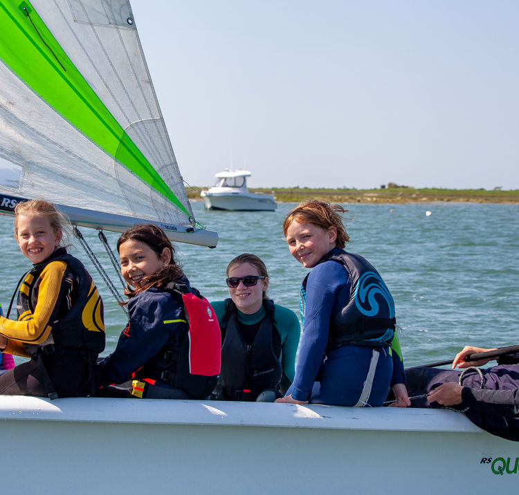 numerous children sailing in a dinghy looking at the camera and smiling
