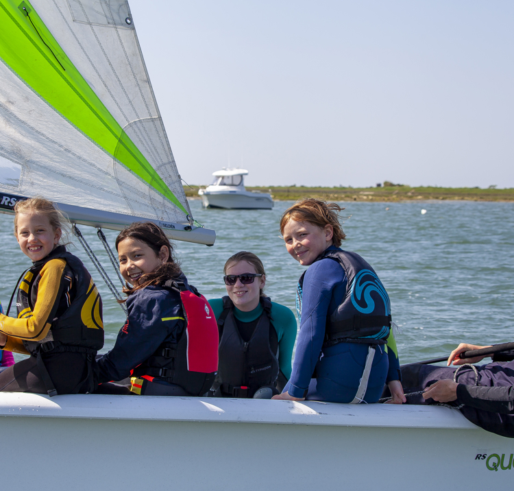 numerous children sailing in a dinghy looking at the camera and smiling