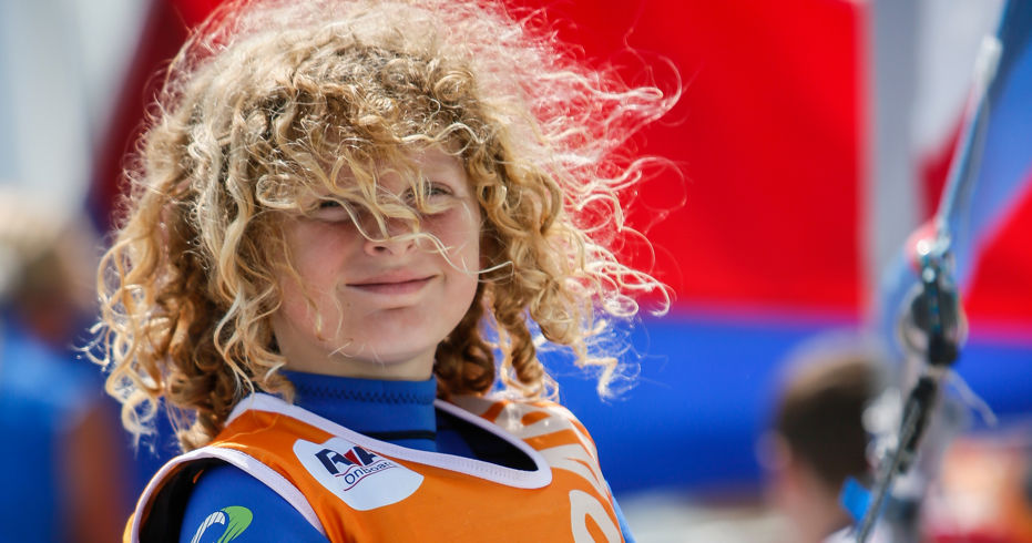 young child with curly hair holding on to ropes. He is wearing an onboard lifejacket