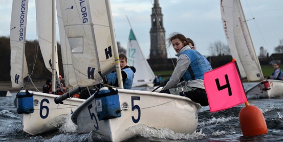 A team from Royal Hospital School sailing towards a mark in close competition with other boats at the RYA Women's Team Racing Championships 2025.