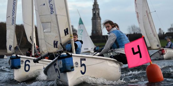 A team from Royal Hospital School sailing towards a mark in close competition with other boats at the RYA Women's Team Racing Championships 2025.