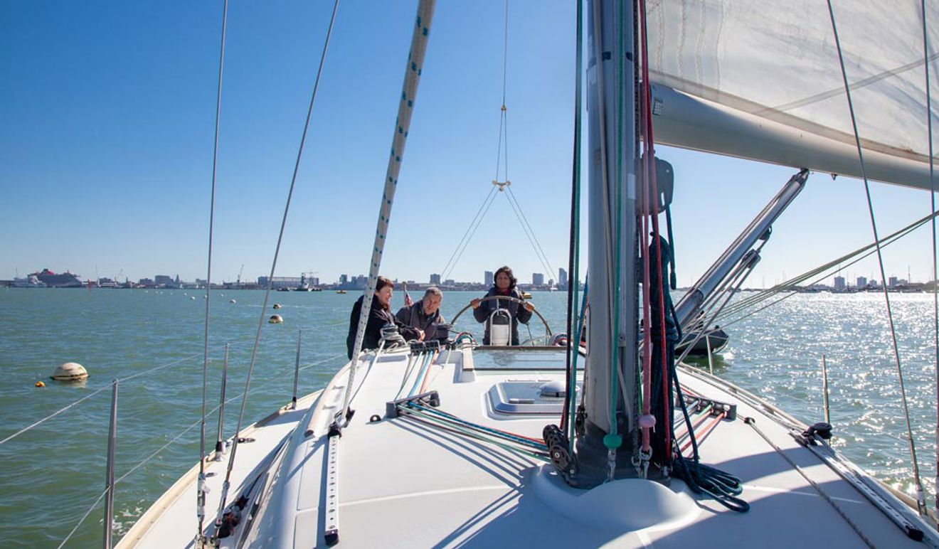 close up of mast cables on board sailing boat, with people in the background and lady steering