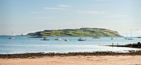 People on the beach in Millport with boats moored in Millport bay, Cumbrae, Scotland