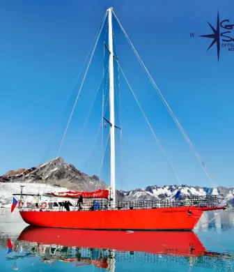 A large red yacht with its sails down, anchored offshore, during an offshore high latitudes adventure with Go West Sailing