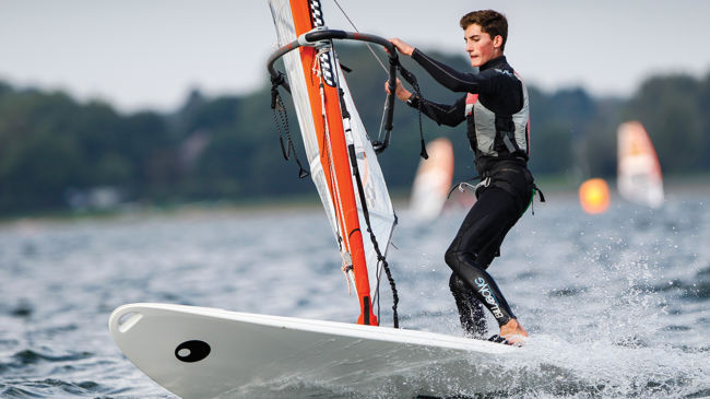 Long shot of boy on windsurf with water splashing