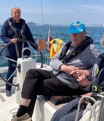An older couple enjoying a day on the water while another lady helms (steers) the yacht with the Disabled Sailing Association in Torquay, Devon