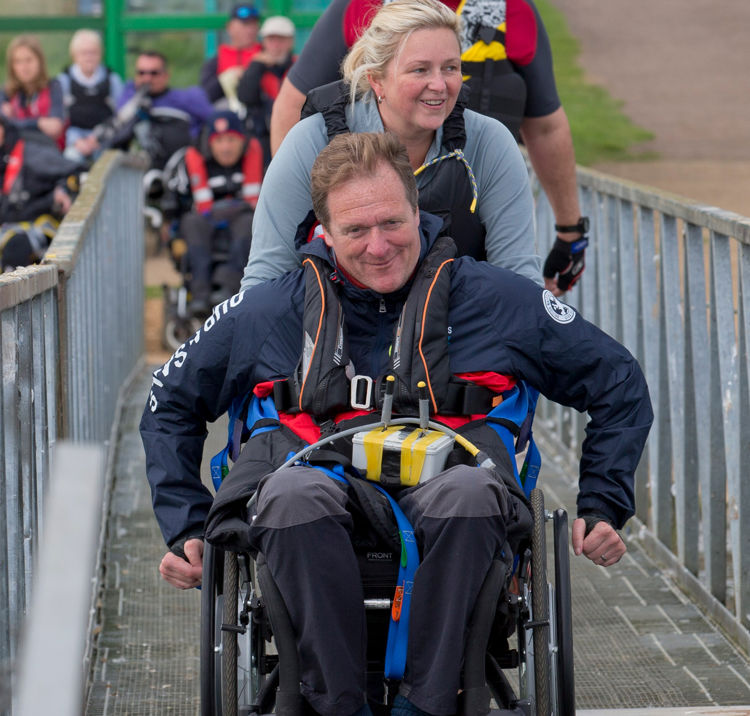 Sailor in wheelchair being helped up to boat