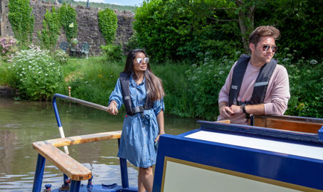 Young couple steering a narrowboat in summer