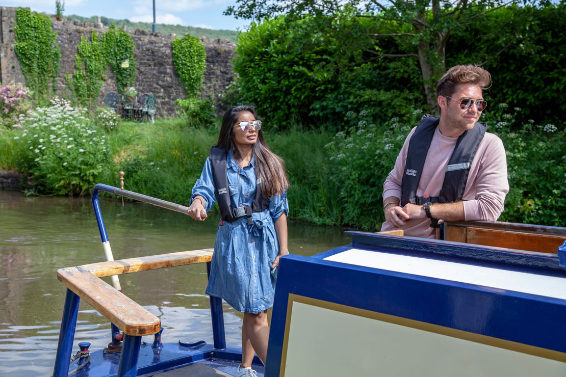 Young couple steering a narrowboat in summer