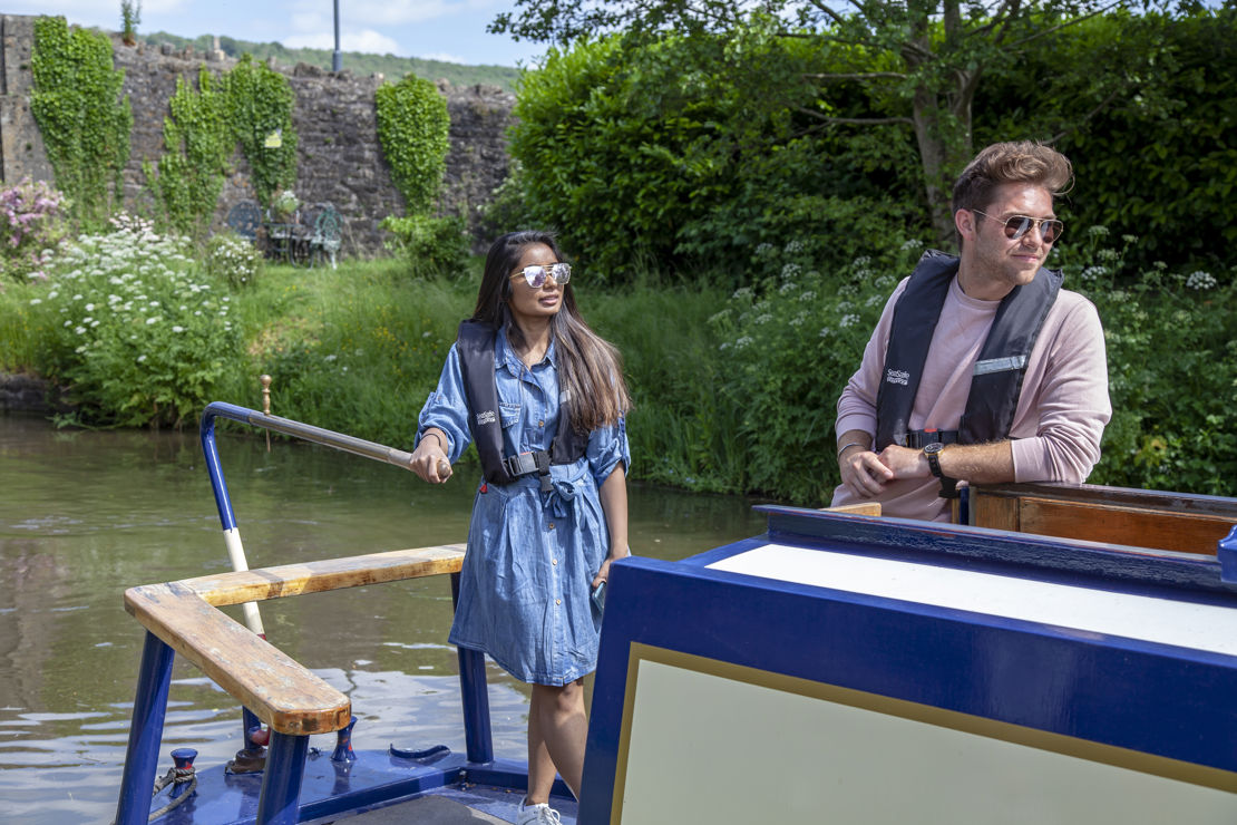 Young couple steering a narrowboat in summer