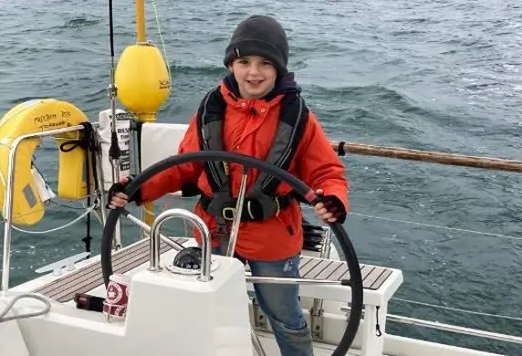 A young child enjoying helming (steering) a sailing yacht with the Disabled Sailing Association in Torquay, Devon