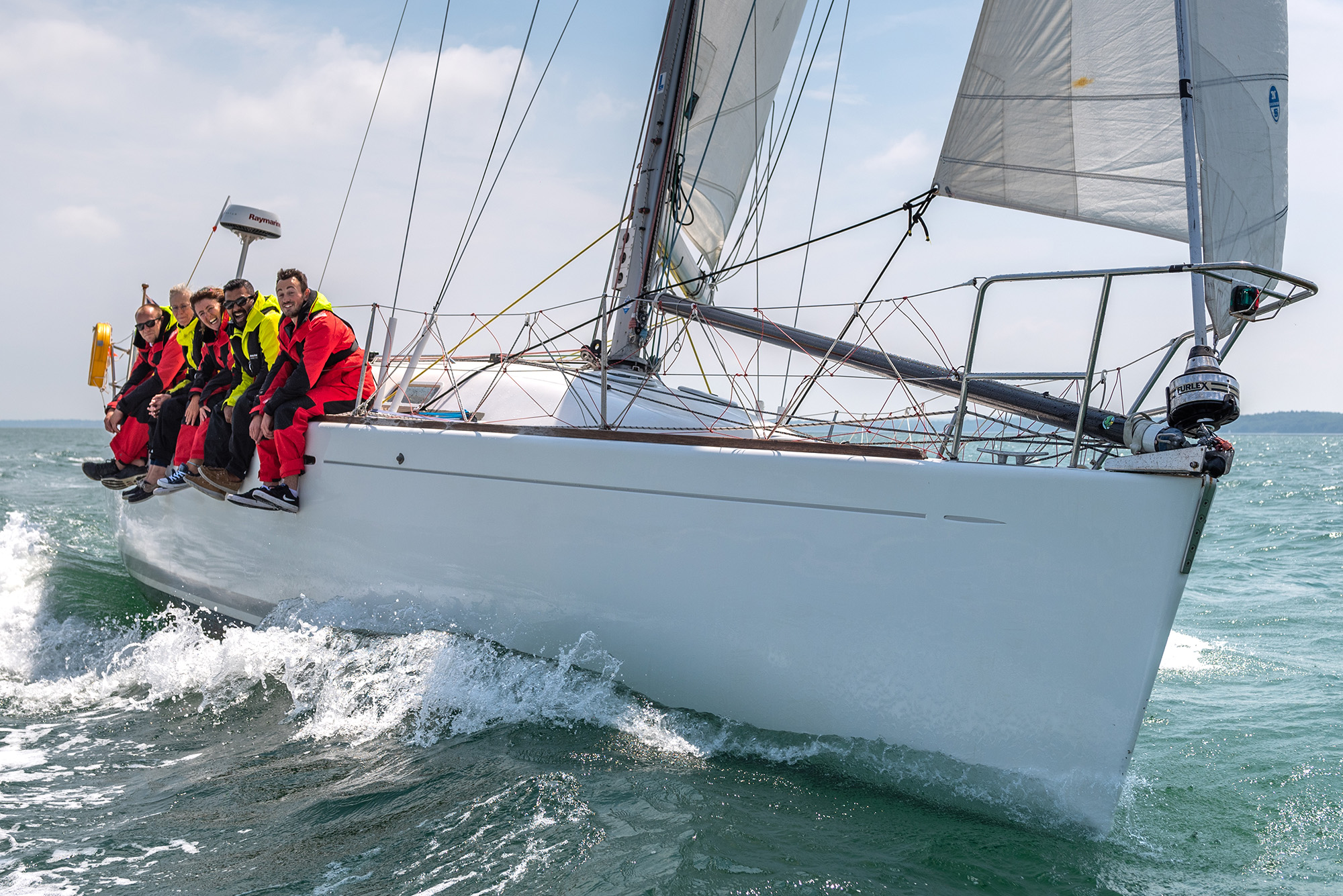 Long shot of crew sat on edge of sailing yacht smiling