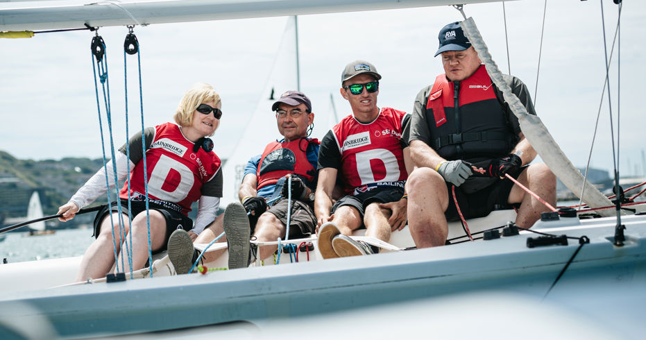 Sailors smiling as they sit over the edge of their boat 