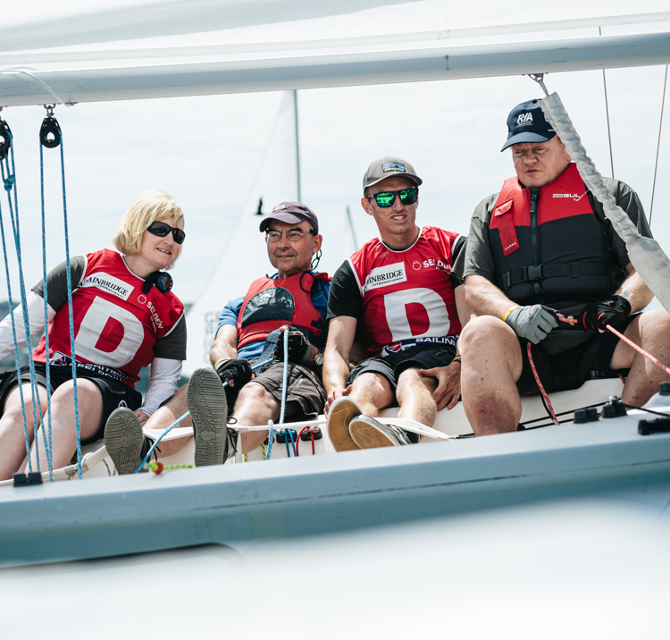 Sailors smiling as they sit over the edge of their boat