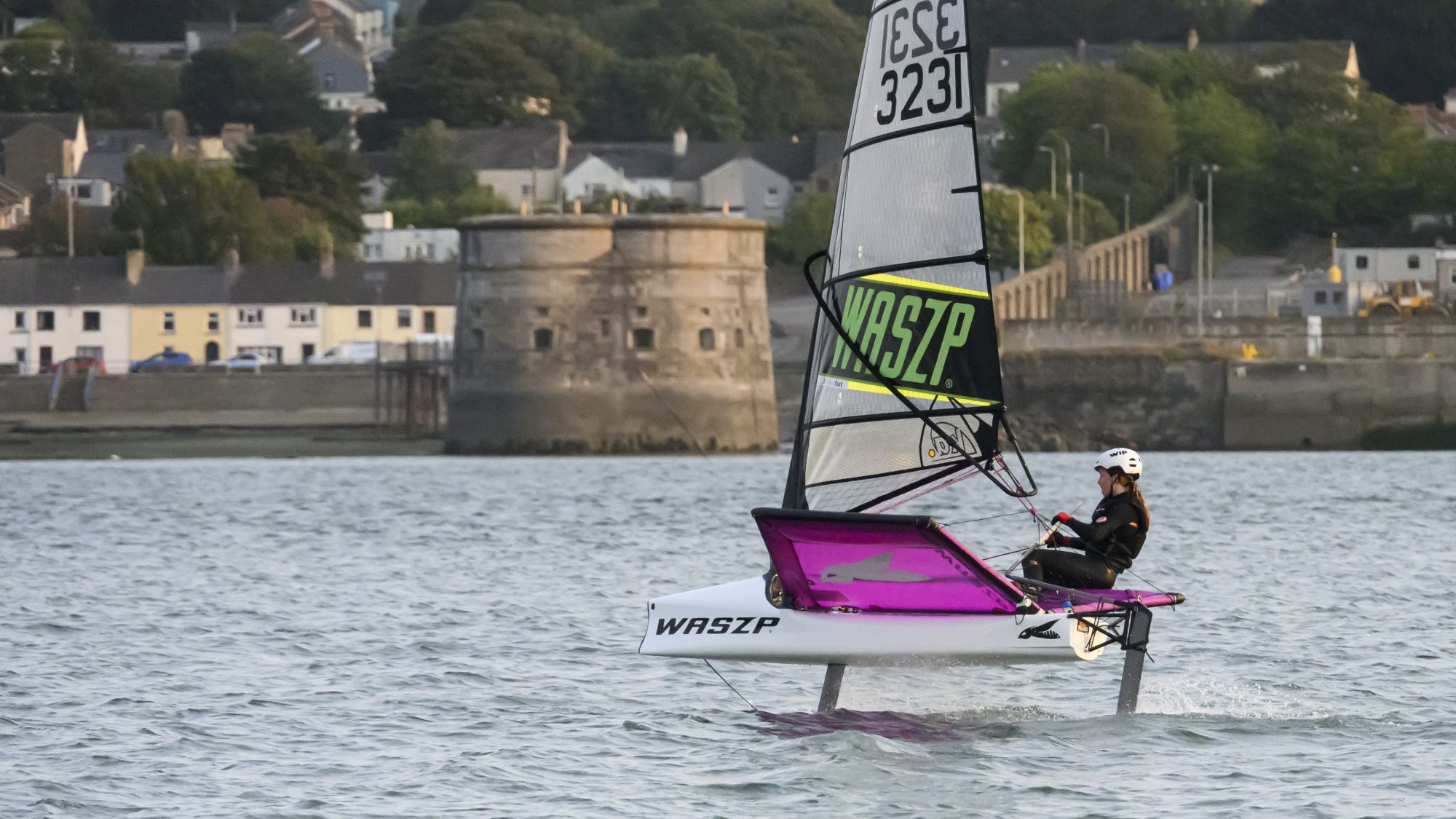 A young Welsh sailor foiling in a Waszp with the shoreline in the background.