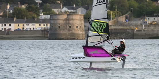 A young Welsh sailor foiling in a Waszp with the shoreline in the background.