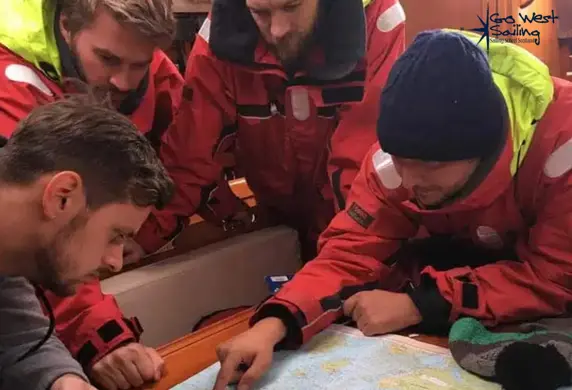 Four men dressed in wet weather gear gathered round a map during their Yachtmaster Skipper training with Go West Sailing