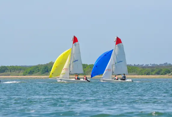 Two small sail boats sailing with yellow and blue spinnakers on the open water from Rockley Point Sailing Centre, Poole, Dorset