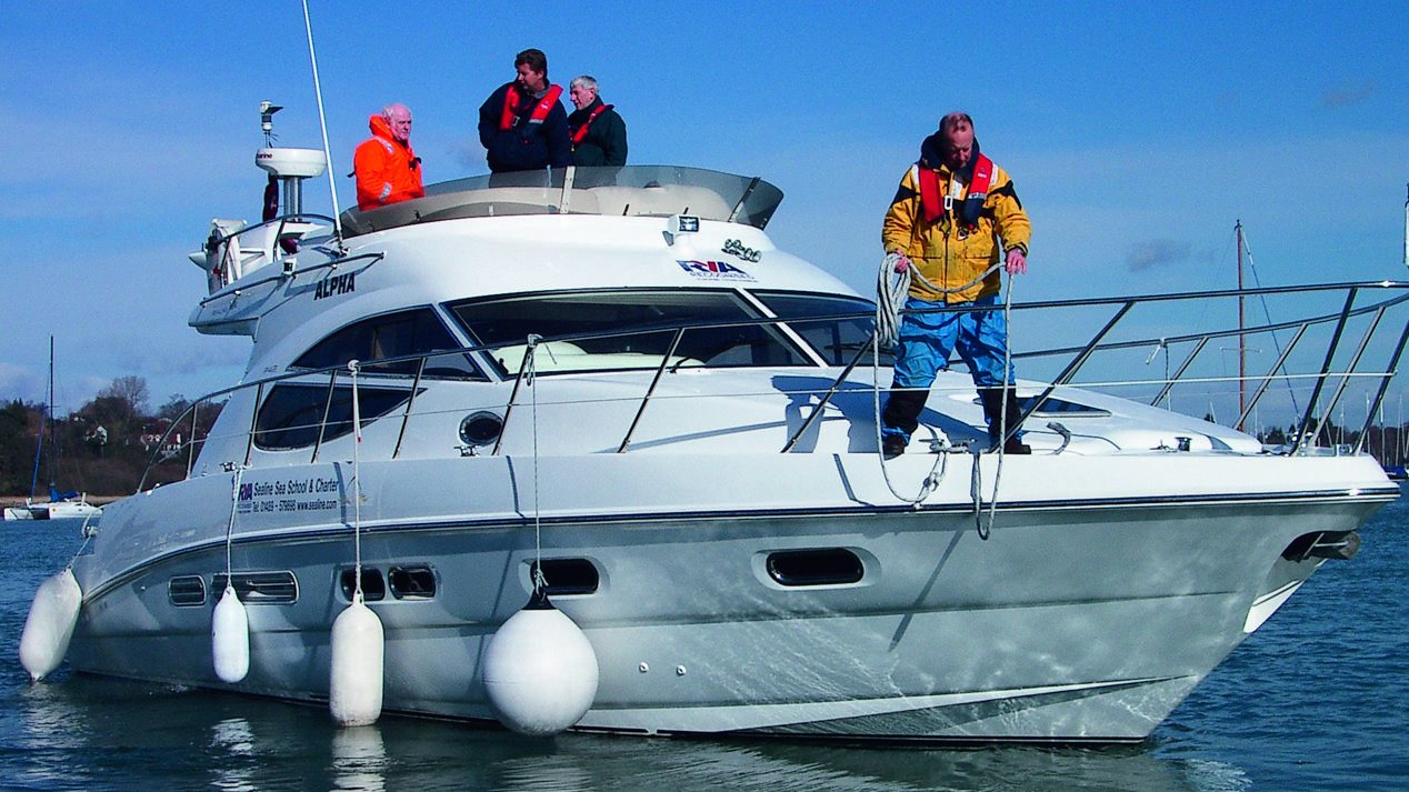 Motor cruiser with buoys hanging from the side and crew stood on deck