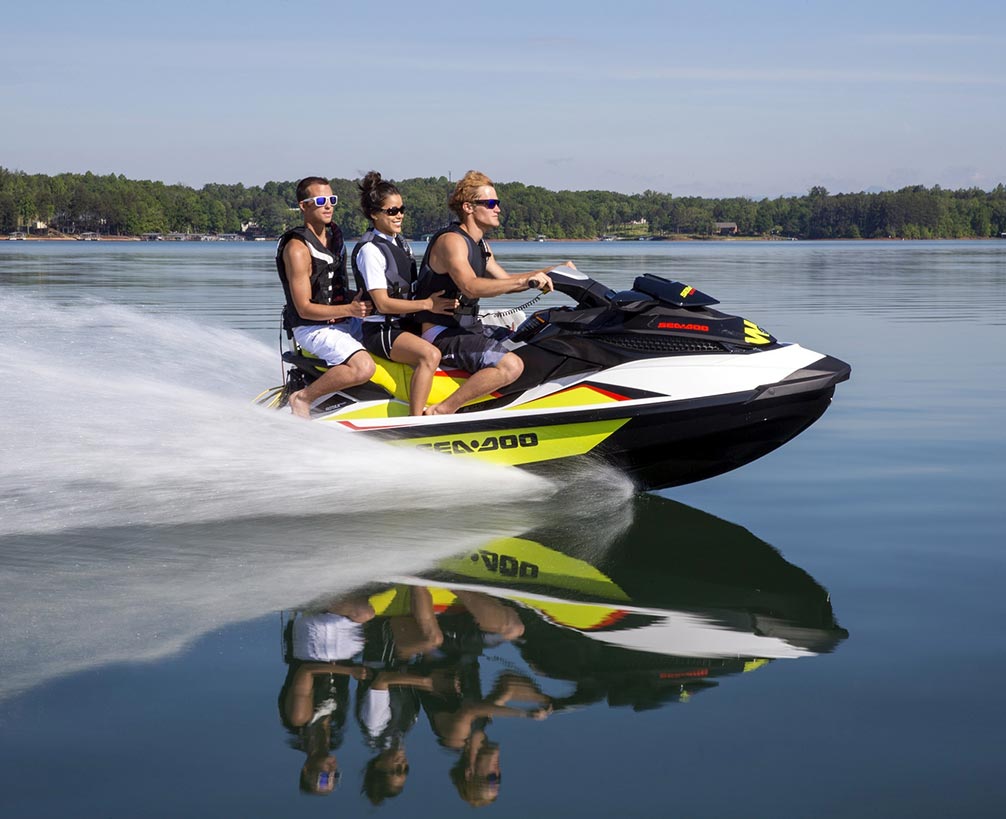 	wide shot of three people on a a personal watercraft going fast on a lake