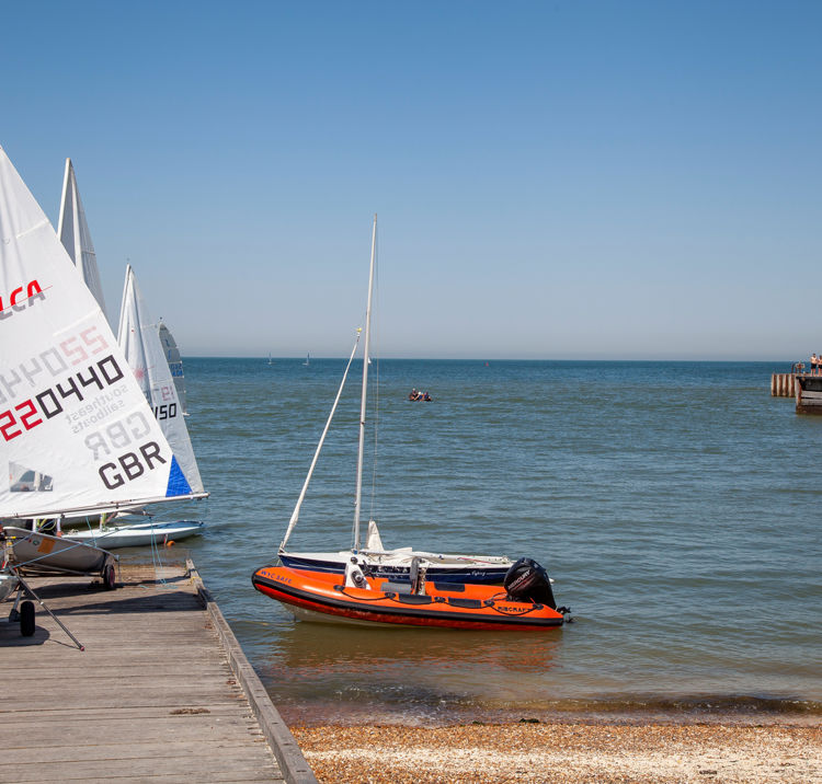 Long shot of orange powerboat and sailing boats near a dock