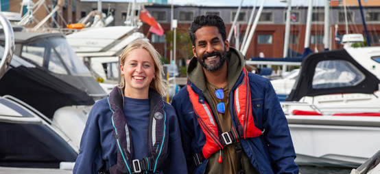 Two sailors at a marina wearing lifejackets ready to go sailing