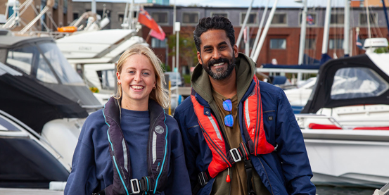 Two sailors at a marina wearing lifejackets ready to go sailing