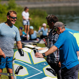 3 men standing around paddle board talking