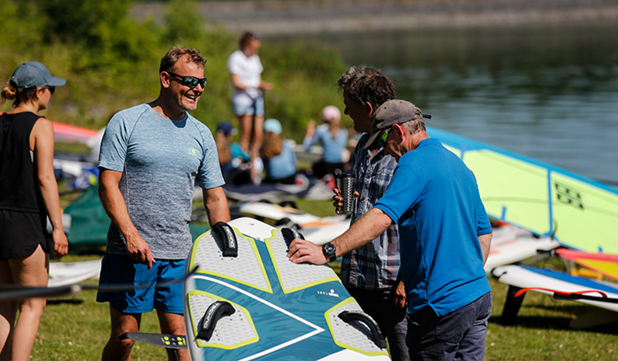 3 men standing around paddle board talking