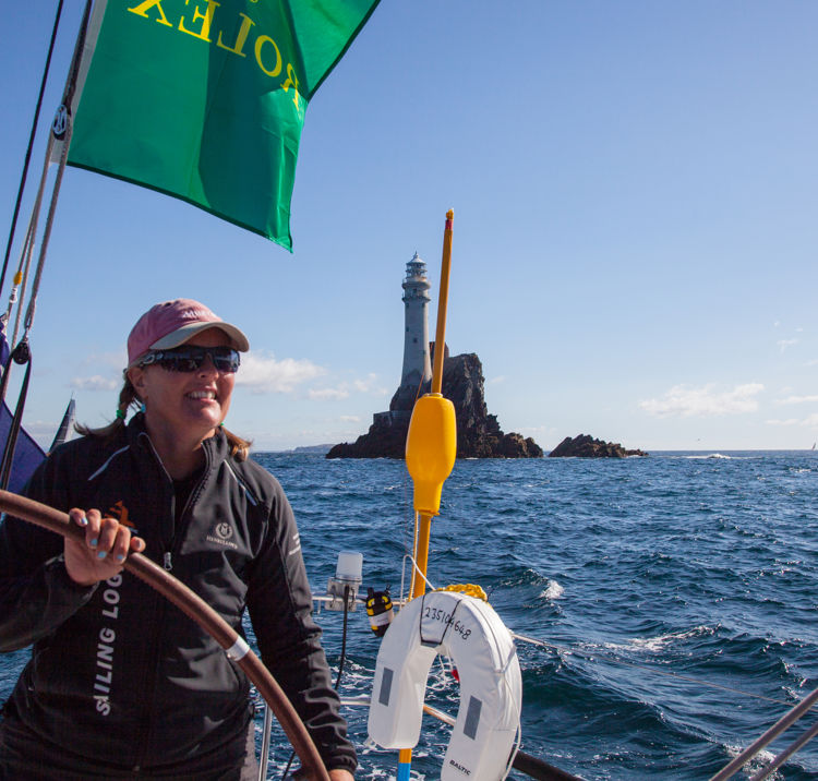 woman steering boat across calm waters with lighthouse in the background