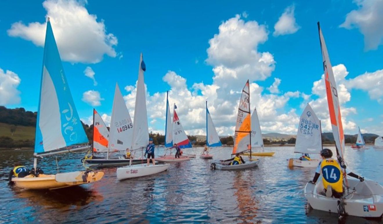 A collection of colourful junior dinghies on the water for an OnBoard Festival with blues skies and fluffy clouds at Bala.