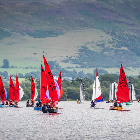 Dinghies with bright red sails floating across rolling hills