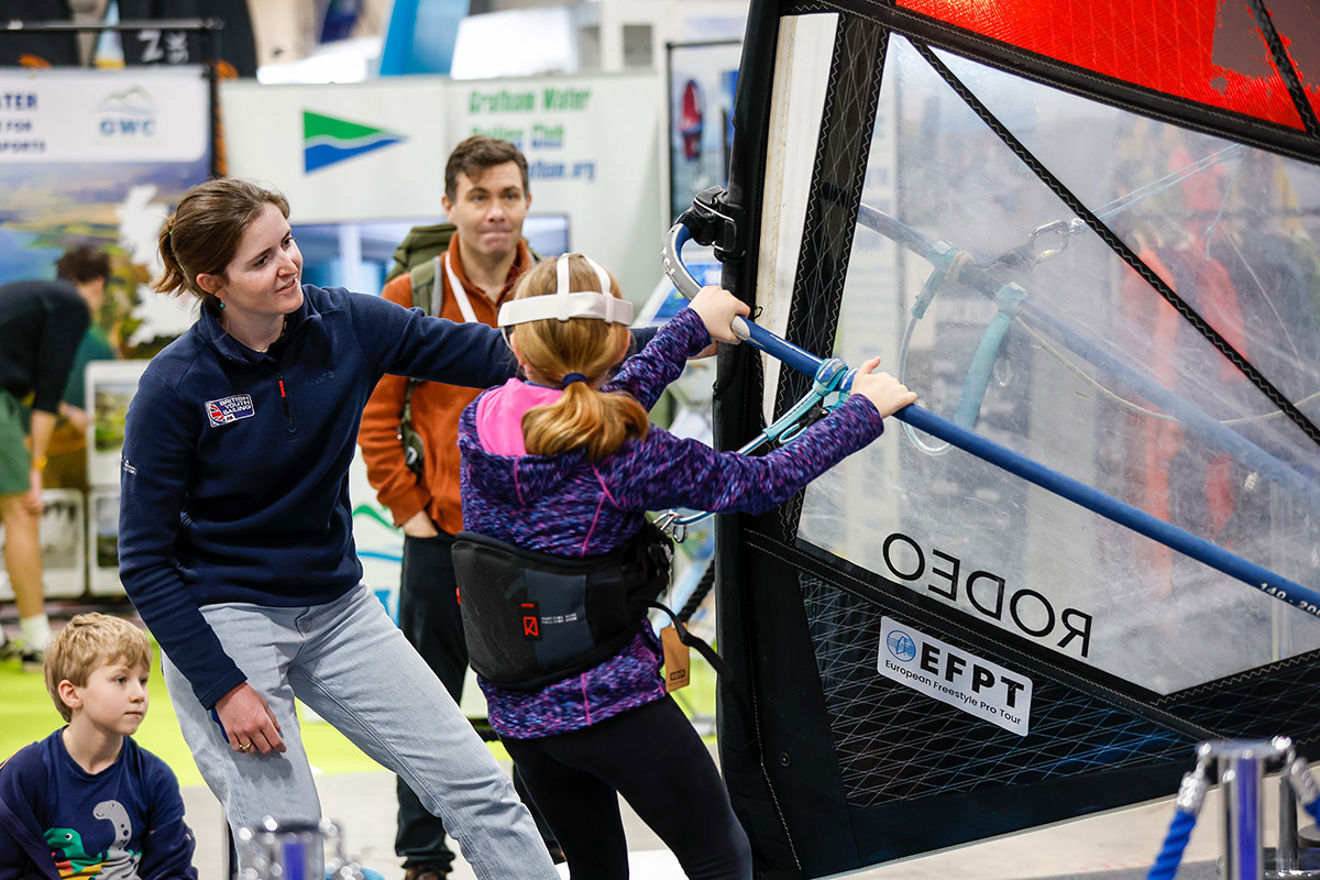 Instructor helps a young sailor on the windsurf simulator at the RYA Dinghy & Watersports Show