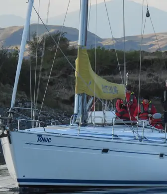 A yacht anchored with its sails away against a shoreline of mountains as the light is fading