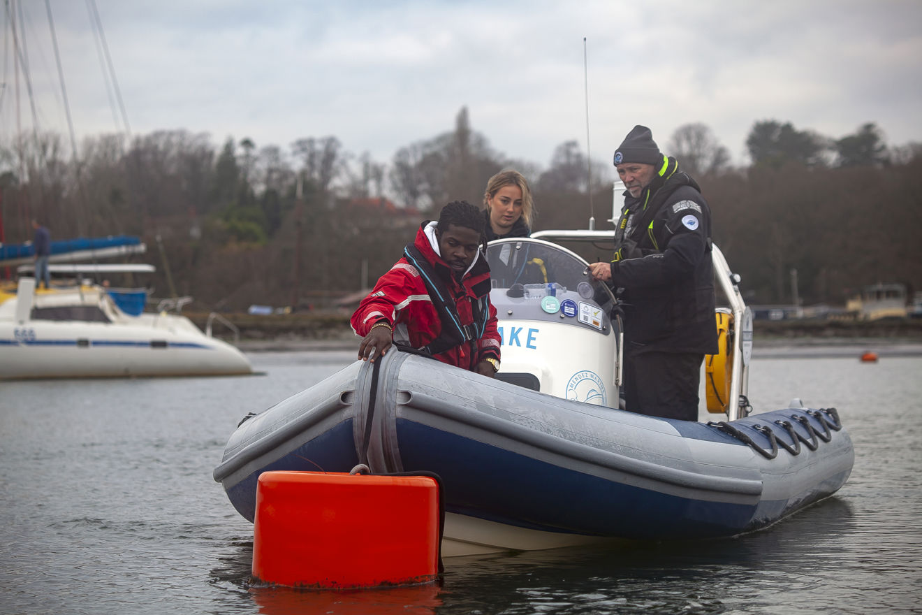 3 people on a powerboat being instructed on how to moore up to a buoy