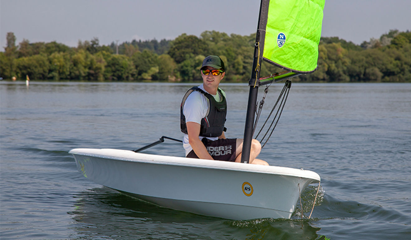 Man on his own sailing in a dinghy wearing sunglasses.