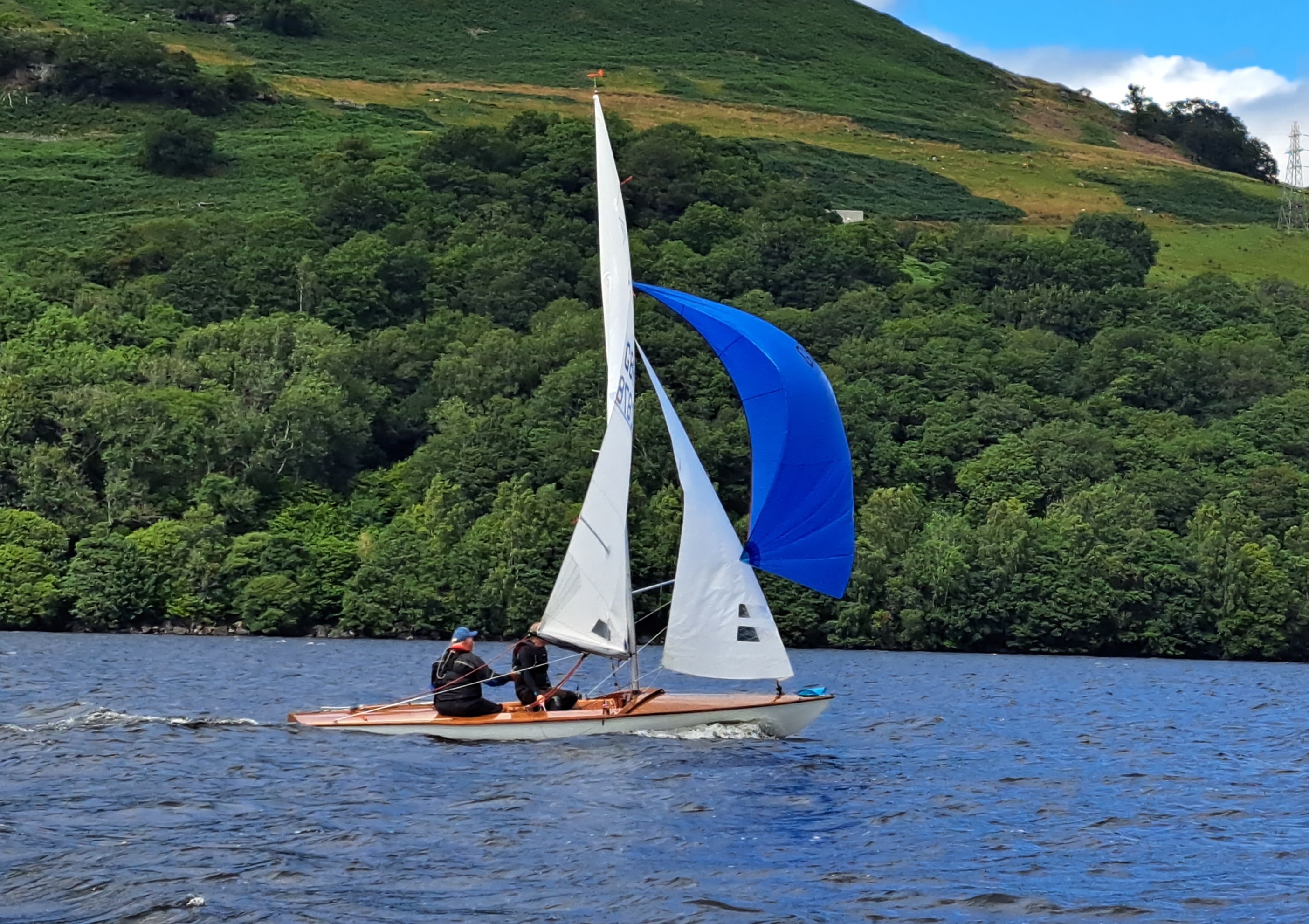 A close up of two people sailing a dinghy with a white main sail and jib and a bright blue spinnaker