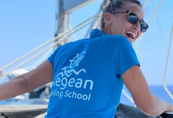 A smiling lady promoting Aegean Sailing School, Aegina, Green on the deck of a sailing yacht on a sunny day