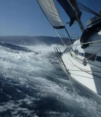 A yacht cutting through the waves against a beautiful blue sky