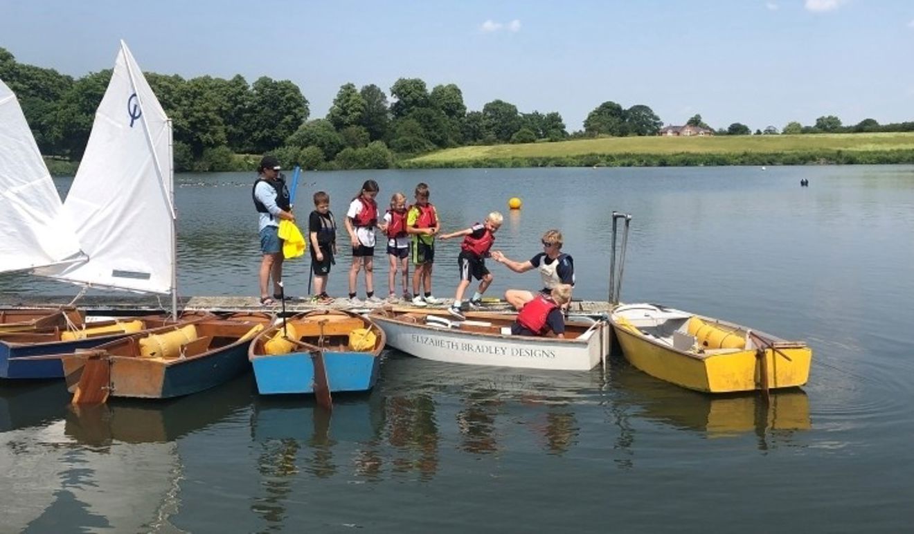 Half a dozen children lining up on a pontoon waiting to climb into children's dinghies with help from an instructor at an All Afloat day hosted by Gresford SC.