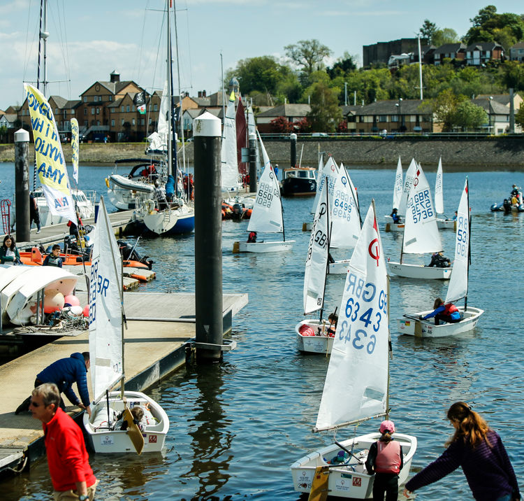 Long shot of lots of sailboats at a dock setting sail