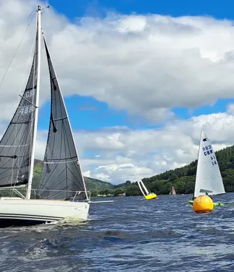 A yacht with two grey sails in the foreground with smaller boats sailing in the background