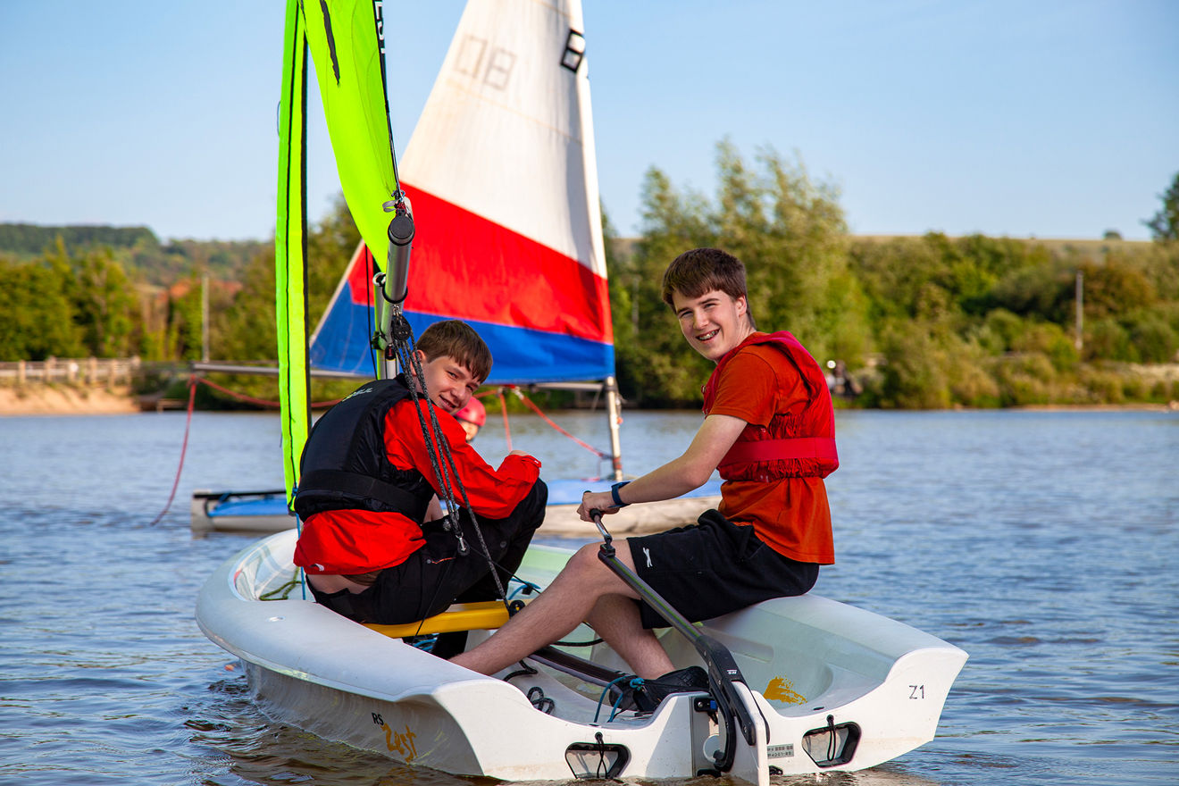 Two teenage boys sailing a dinghy, smiling at the camera